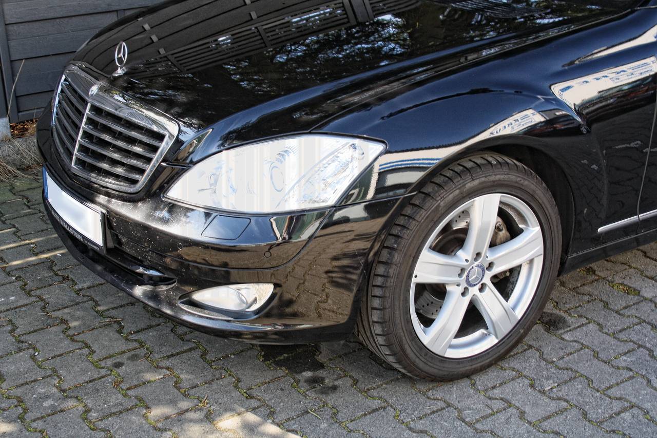 Schwarzer Limousinen-Vorderteil, geparkt auf gepflastertem Parkplatz, Mercedes-Emblem sichtbar auf Motorhaube.