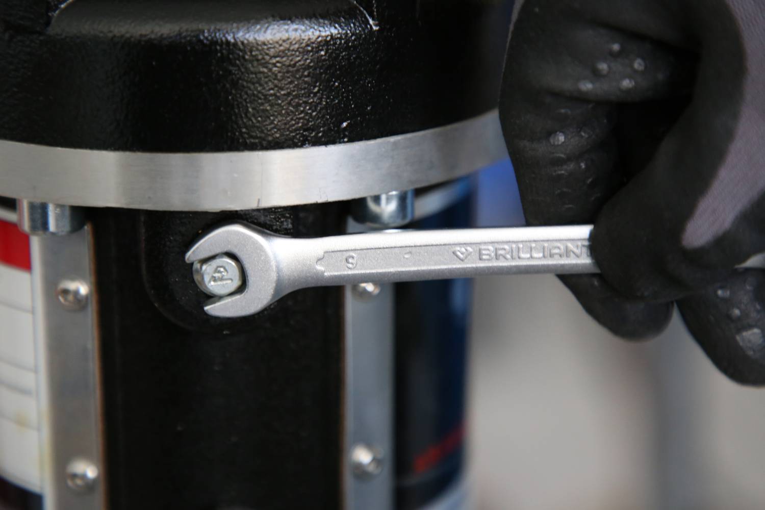 Eine Hand trägt einen Handschuh und hält einen Schraubenschlüssel, um eine Schraube an einer Metallmaschine festzuziehen.