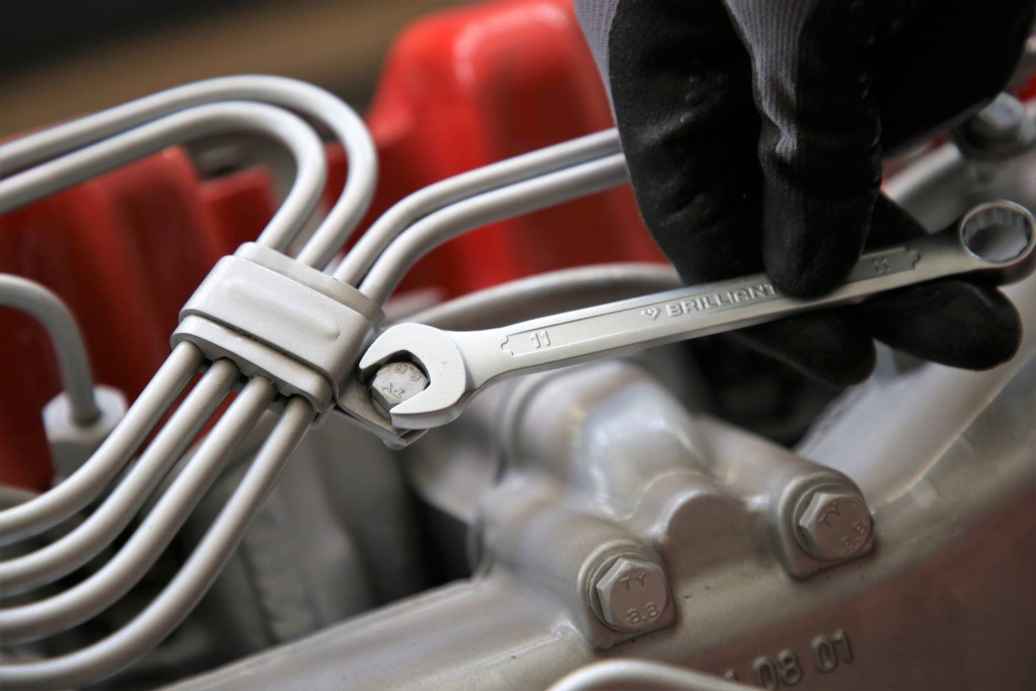 Hand in schwarzem Handschuh hält einen Schraubenschlüssel, der an einem Gewinde in einem Maschinenteil arbeitet.