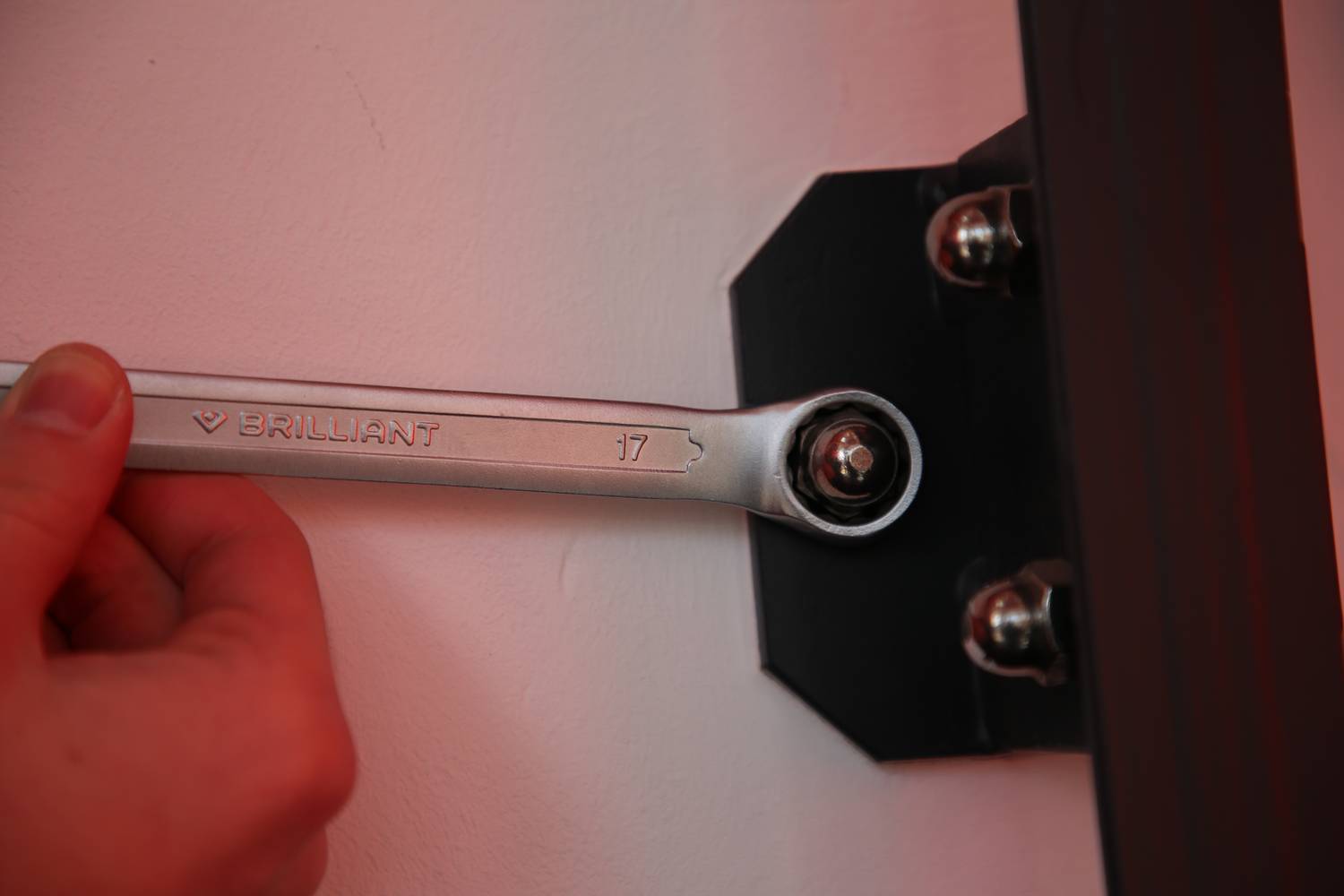 Eine Person hält einen Schraubenschlüssel, um eine Schraube an einer schwarzen Halterung festzuziehen. Der Schraubenschlüssel zeigt die Größe 17.