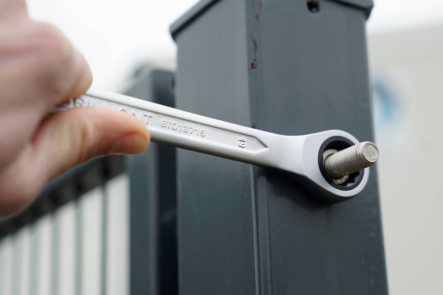Nahaufnahme eines Schraubenschlüssels, der eine Mutter an einem Metallpfosten festzieht, gehalten von einer Hand. Technik oder Konstruktion.