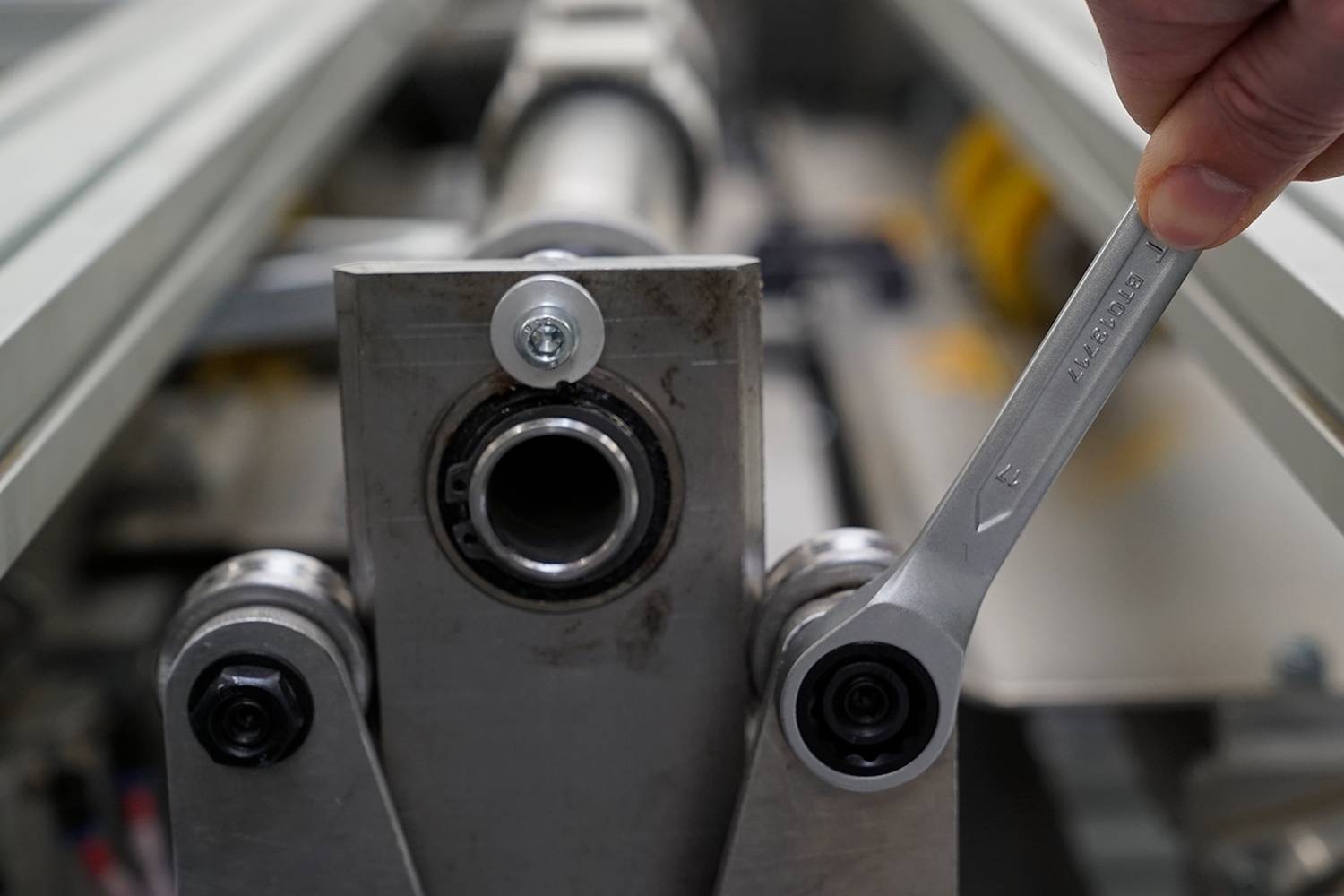 Eine Hand benutzt einen Schraubenschlüssel, um eine Schraube an einer Maschine zu drehen. Der Fokus liegt auf der Mechanik der Maschine.