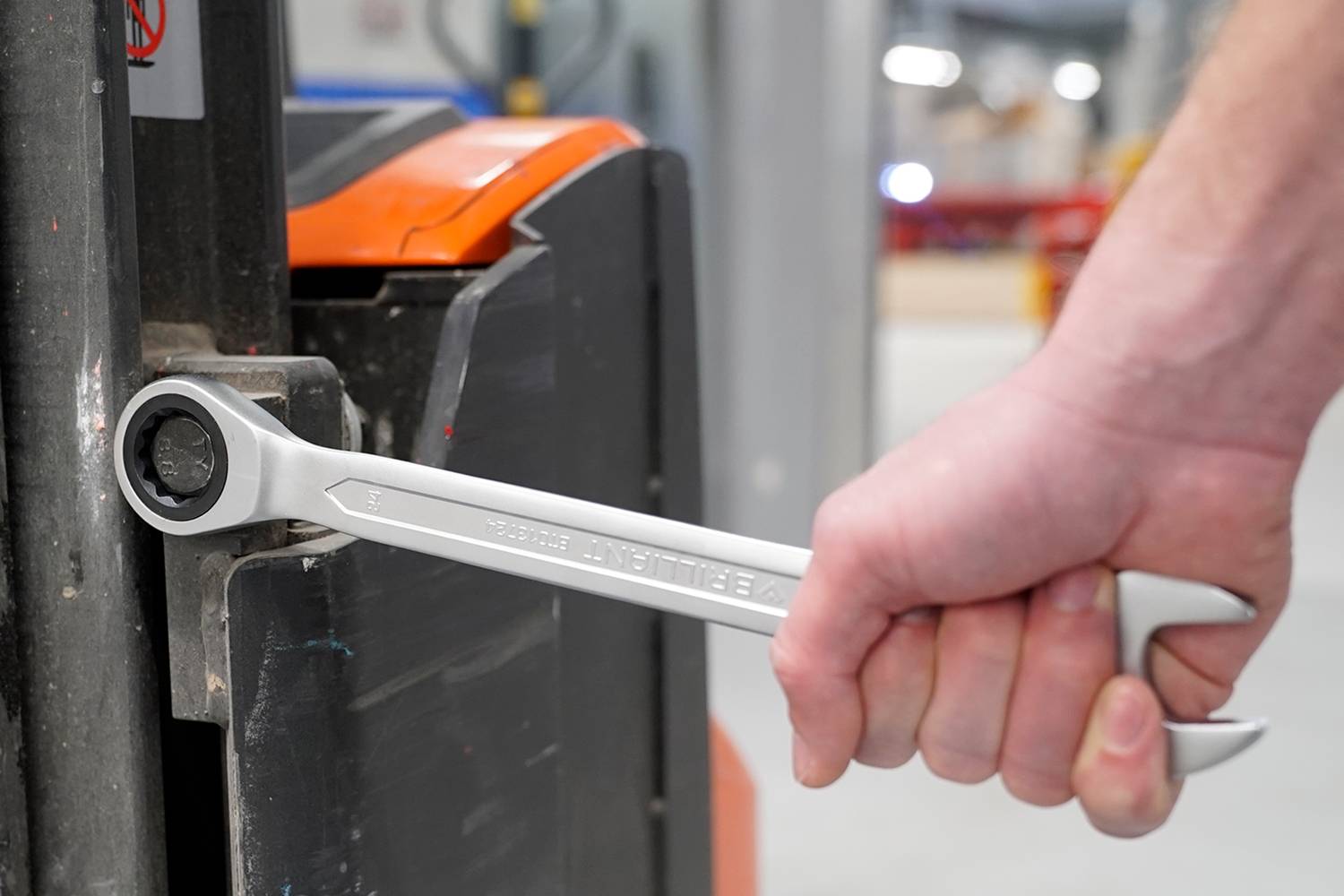 Eine Person zieht mit einem großen Schraubenschlüssel eine Schraube an einem schwarzen Metallobjekt, möglicherweise Teil einer Maschine, fest.