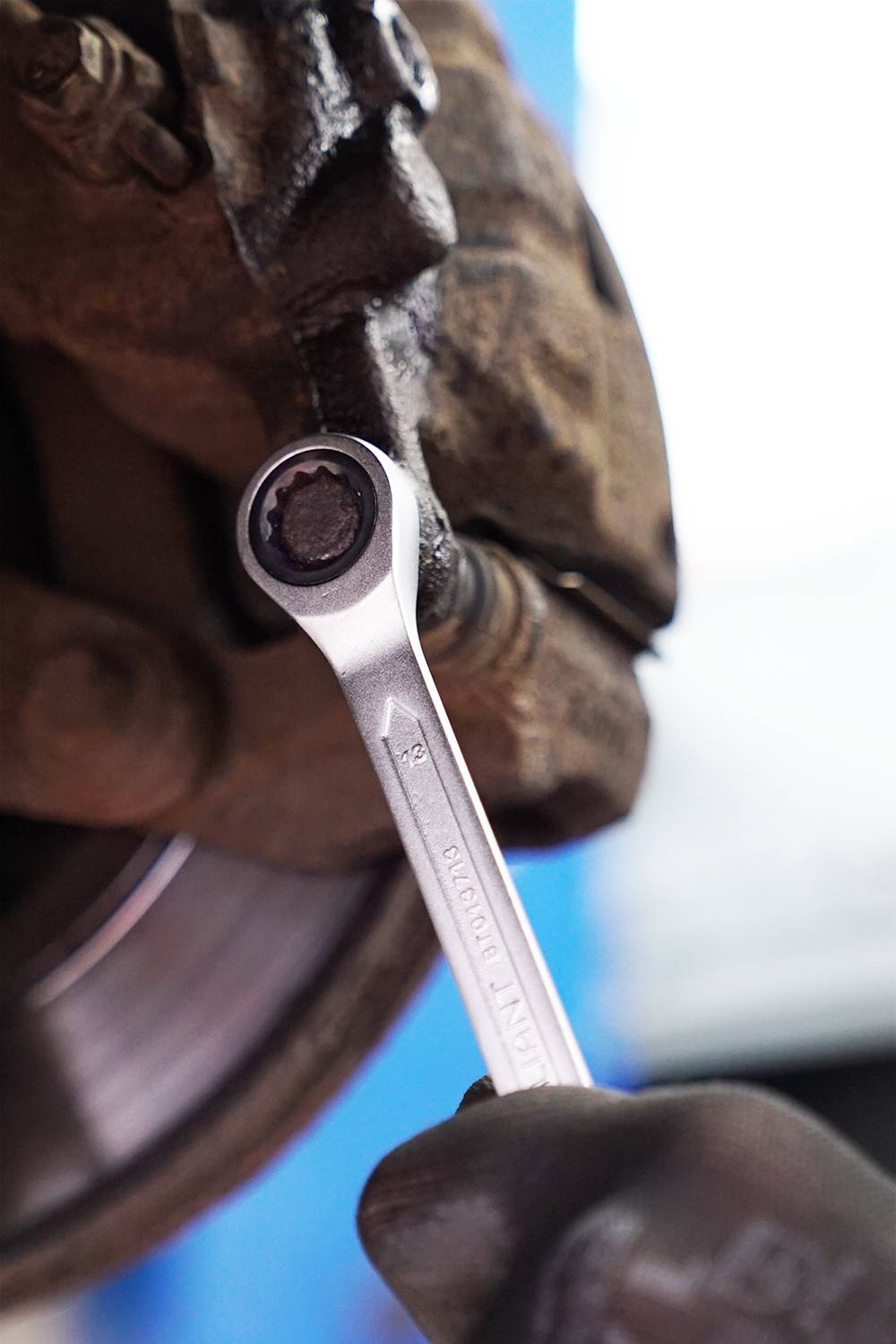 Eine Hand mit Handschuh hält einen Schraubenschlüssel und arbeitet an einer Fahrzeugbremse, Fokus auf Reparatur.