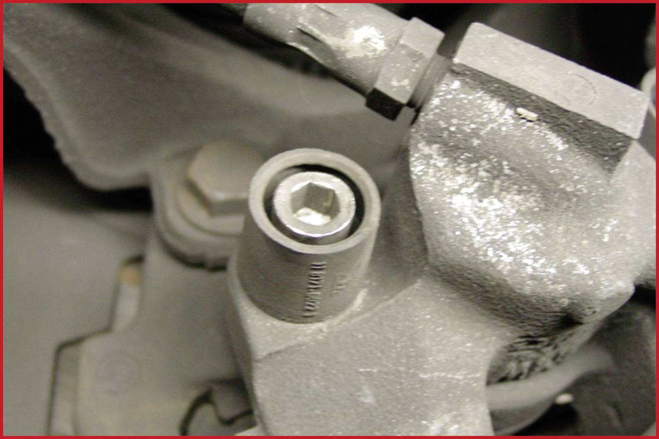 Nahaufnahme einer verschmutzten Sechskantschraube in einem mechanischen Gerät. Die Umgebung zeigt abgenutzte Metallteile.