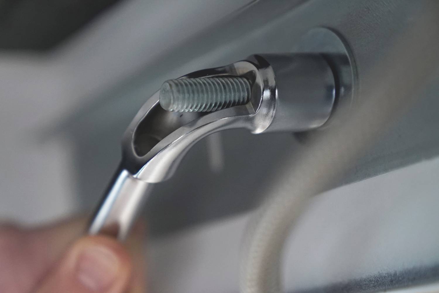 Eine Nahaufnahme einer Hand, die einen silbernen Schraubenschlüssel benutzt, um eine Schraube an einem Metallstück zu befestigen.