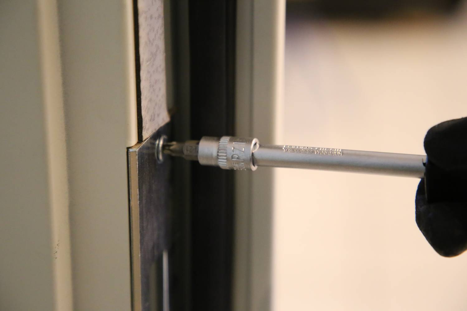 Eine Person zieht mit einem Schraubenzieher die Schraube an einem Türrahmen fest, möglicherweise bei der Installation oder Reparatur.