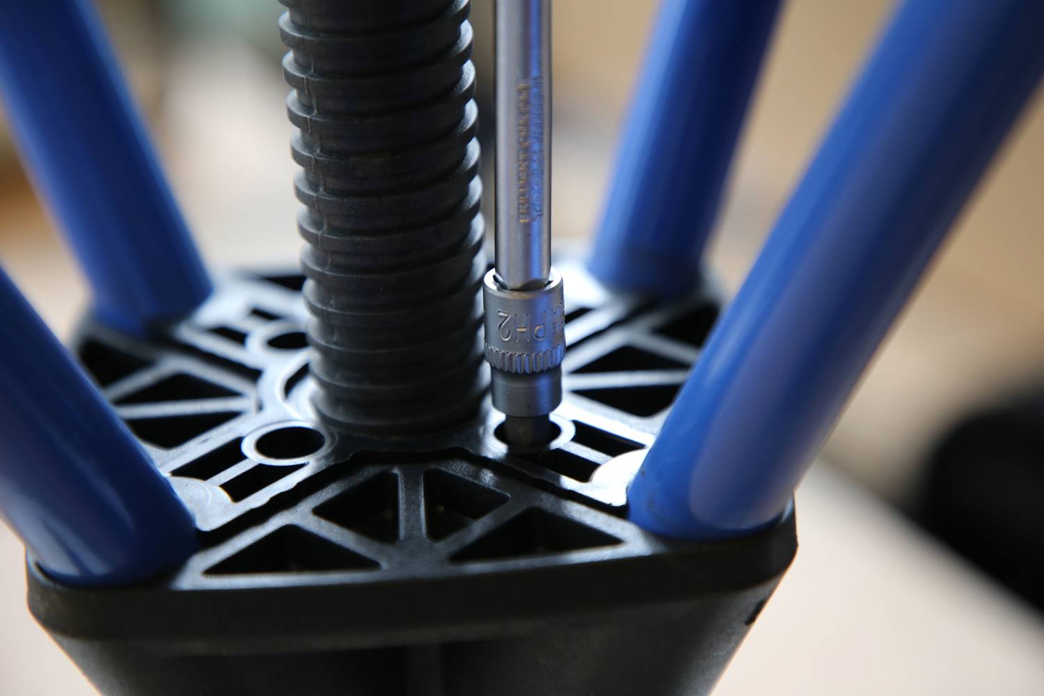 Nahaufnahme eines Metallwerkzeugs, das in einem schwarzen, runden Werkstück mit blauen Armen eingesetzt wird. Fokus auf die Anwendung des Werkzeugs.