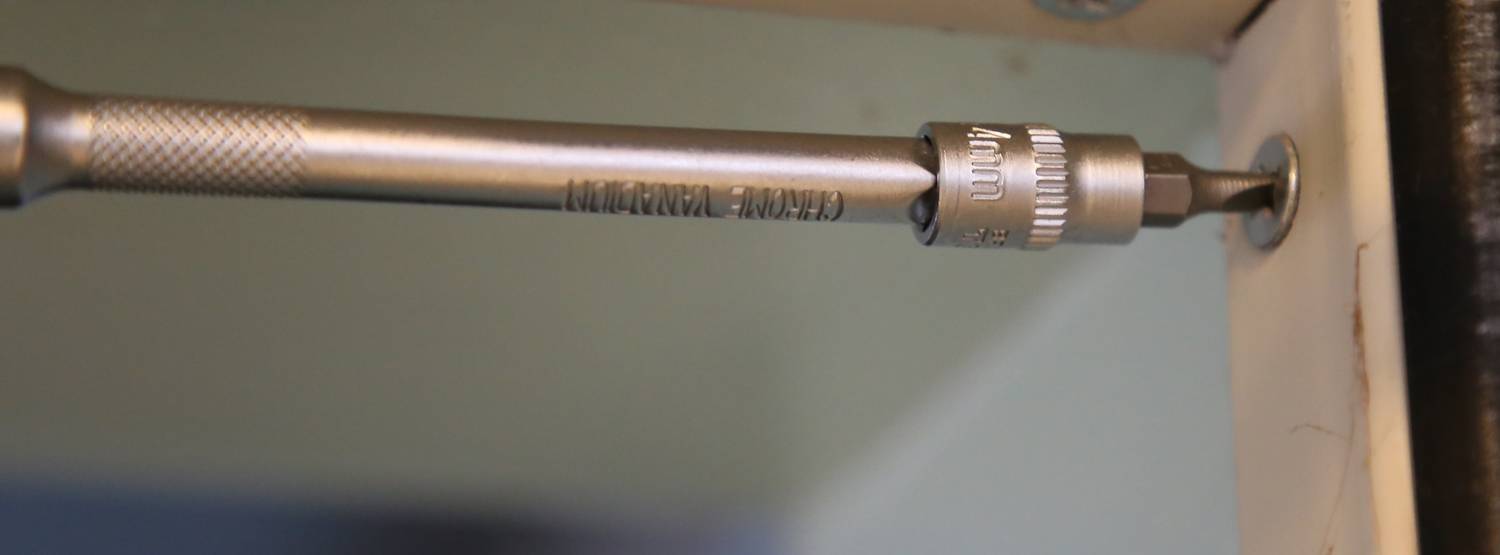 Nahaufnahme eines Schraubenziehers, der eine Schraube in ein Holzstück dreht. Der Schraubenzieher ist metallisch und strukturiert.