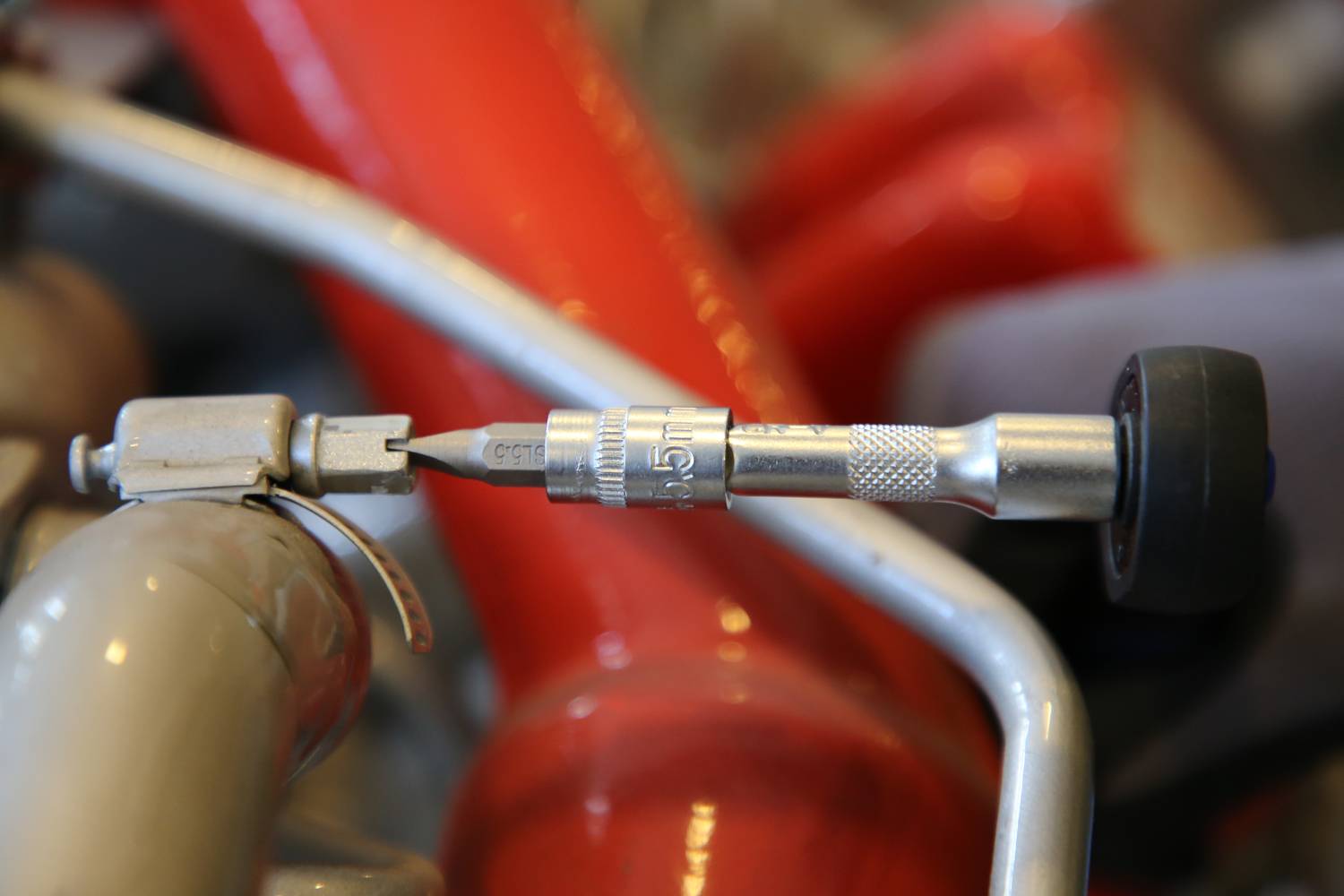 Nahaufnahme eines Drehmomentschlüssels, der an einer Metallverschraubung arbeitet. Hintergrund zeigt unscharfe, rote Röhren.