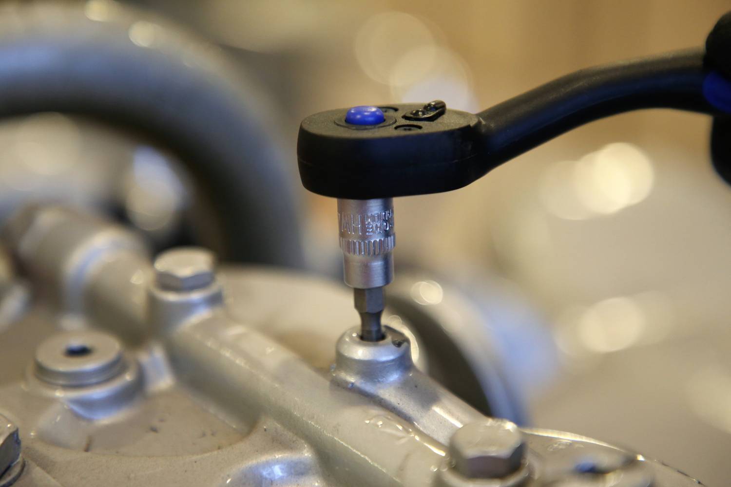 Schraubenschlüssel zieht Schraube an Motor fest. Nahaufnahme zeigt Prozess der Befestigung in Werkstattumgebung.