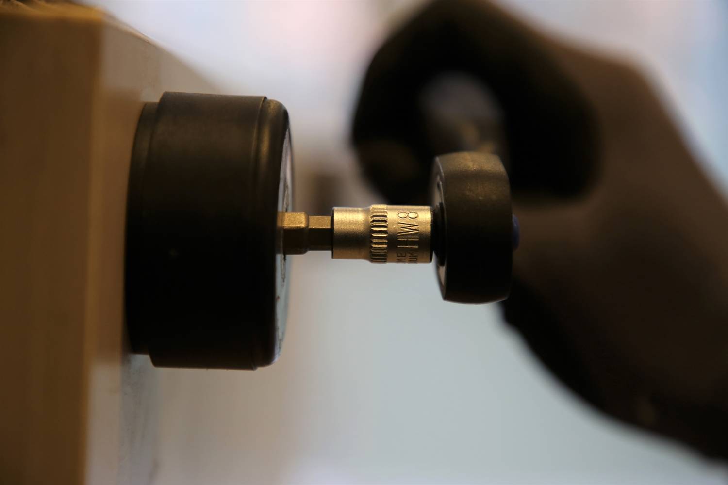 Hand mit schwarzem Handschuh dreht ein Messgerät. Der Fokus liegt auf dem Werkzeug und der Aktion.