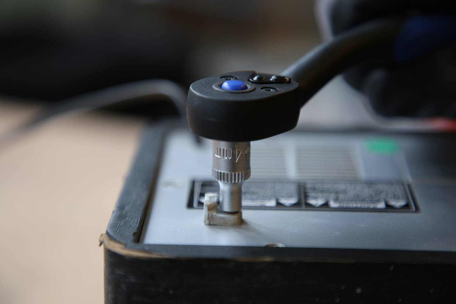 Eine Hand hält einen Schraubenschlüssel, der eine Schraube an einer Batterie festzieht. Fokus liegt auf dem Arbeitsvorgang.