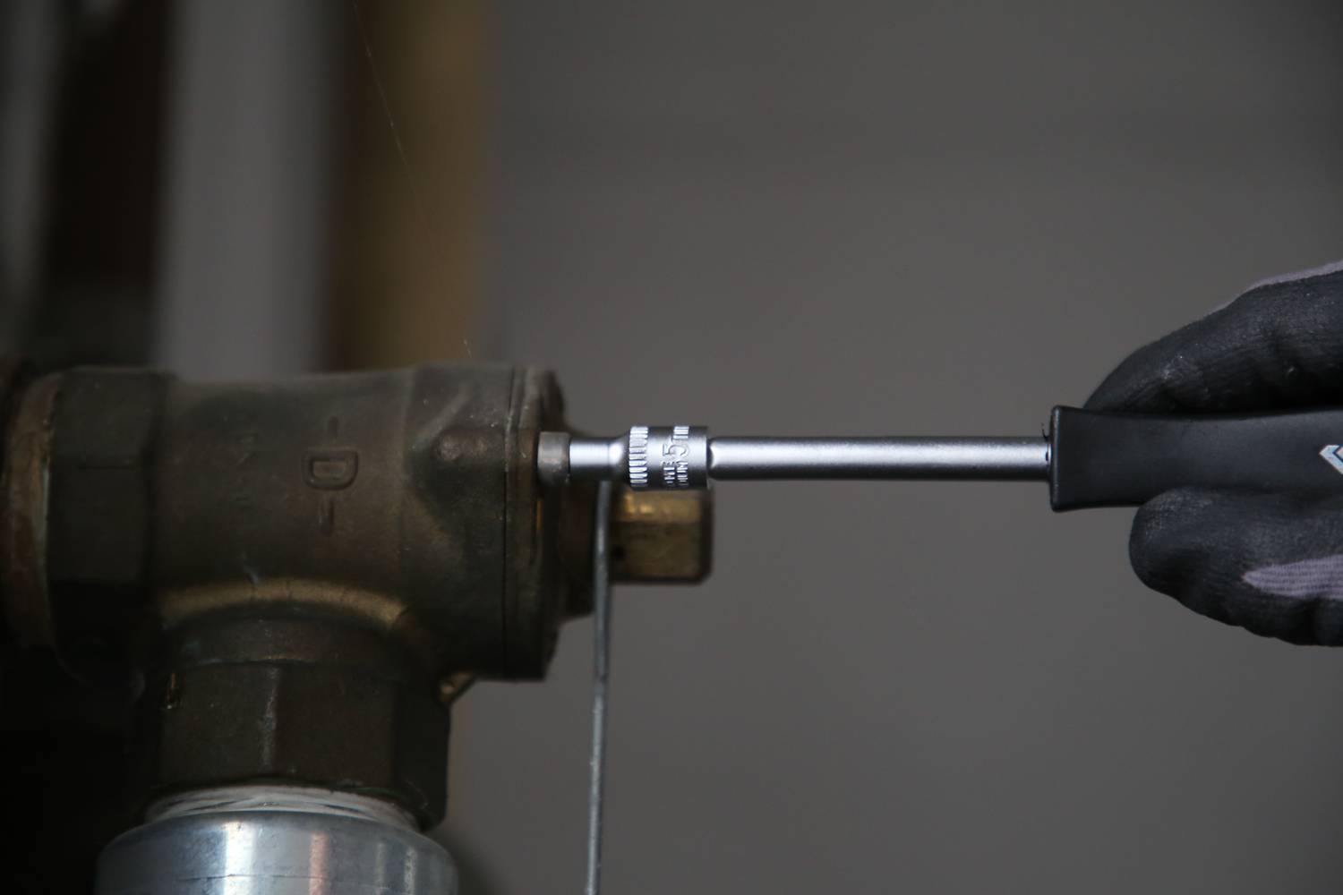 Eine Person zieht mit einem Schraubenschlüssel eine Schraube an einem Metallrohr an.