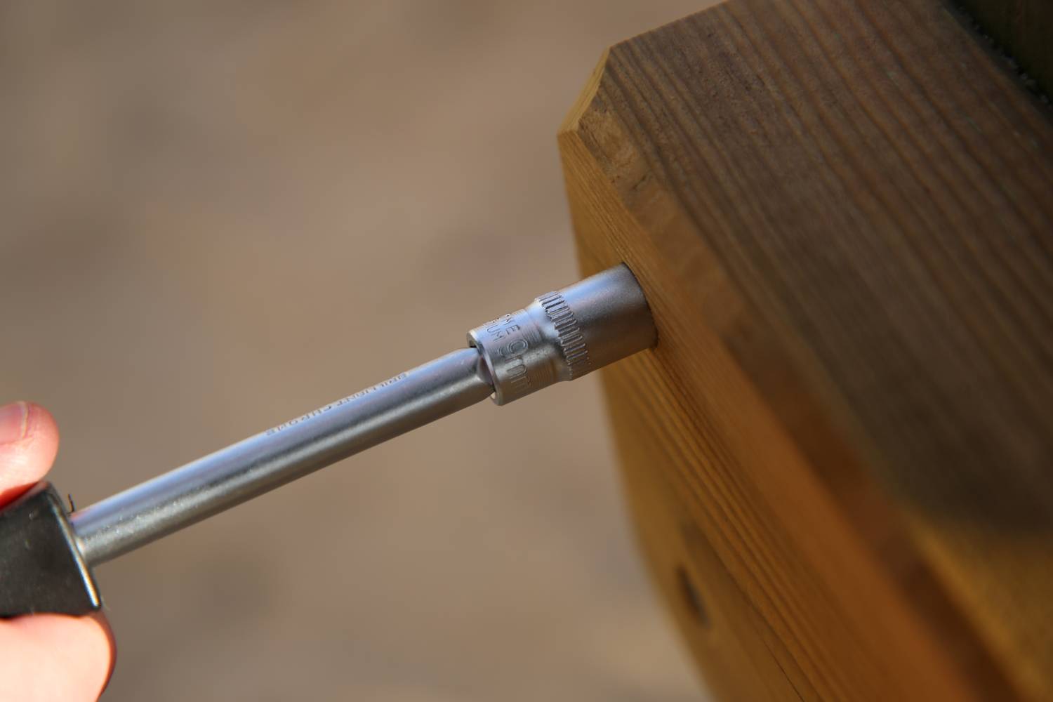 Nahaufnahme eines Schraubenschlüssels, der in einen Holzbalken geschraubt wird. Die Hand eines Menschen hält den Griff des Werkzeugs.