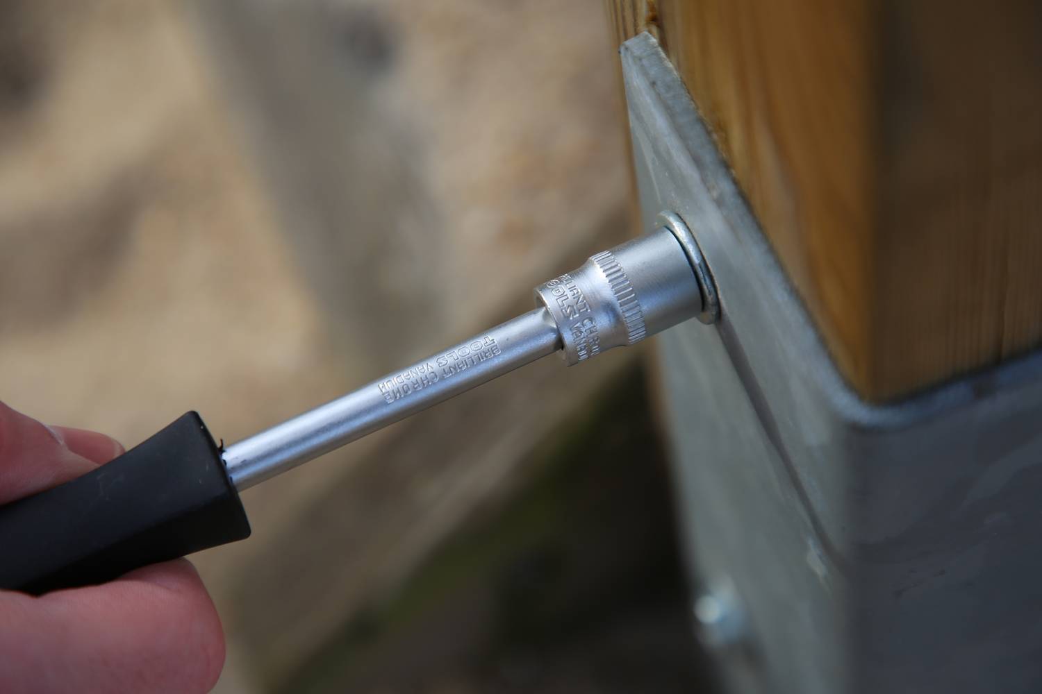 Eine Hand hält einen Schraubenschlüssel und zieht eine Schraube an einem Holzstruktur fest.