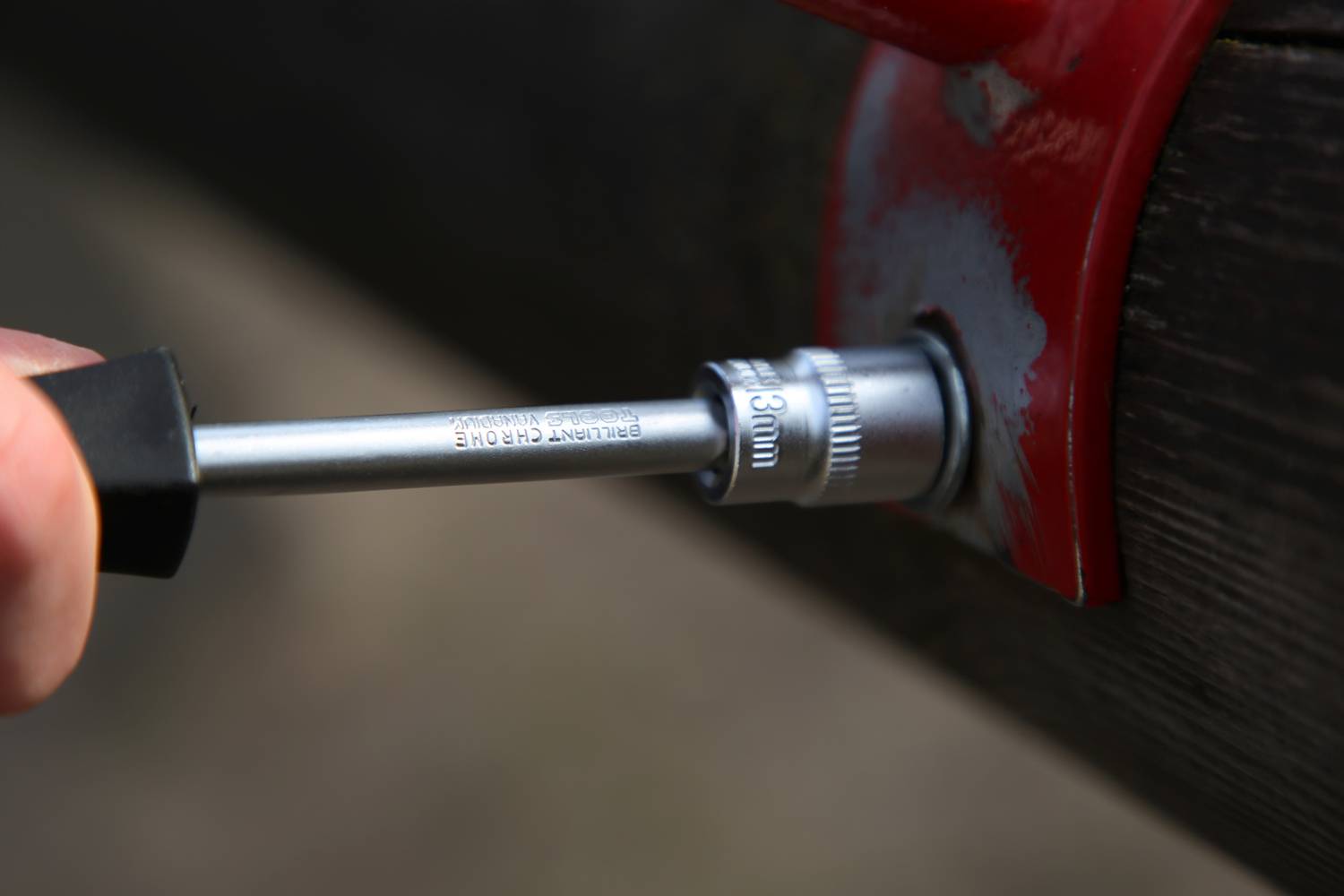 Ein Metallrohr wird mit einem Steckschlüssel angezogen. Der Aufsatz zeigt '20mm'. Eine rote Halterung befindet sich am Rohr.