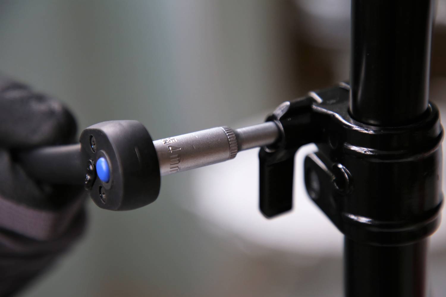 Nahaufnahme einer Hand, die mit einem Inbusschlüssel eine Schraube anzieht, um ein schwarzes Stativ zu sichern. Fokus auf Werkzeug und Schraube.