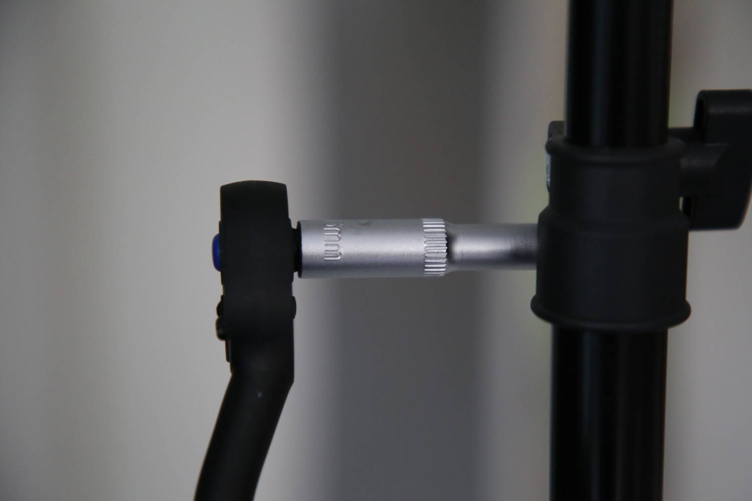 Ein schwarzer Mikrofonarm mit einem silbernen verstellbaren Gelenk ist an einem Ständer montiert und vor einem neutralen Hintergrund platziert.