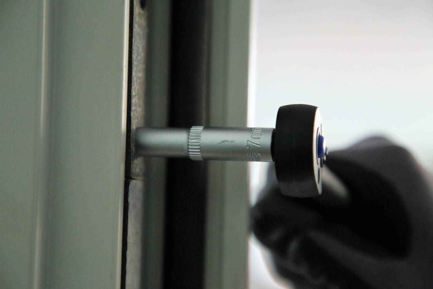 Hand in schwarzem Handschuh dreht ein Werkzeug an einem Fensterrahmen, möglicherweise für Montage- oder Reinigungsarbeiten.
