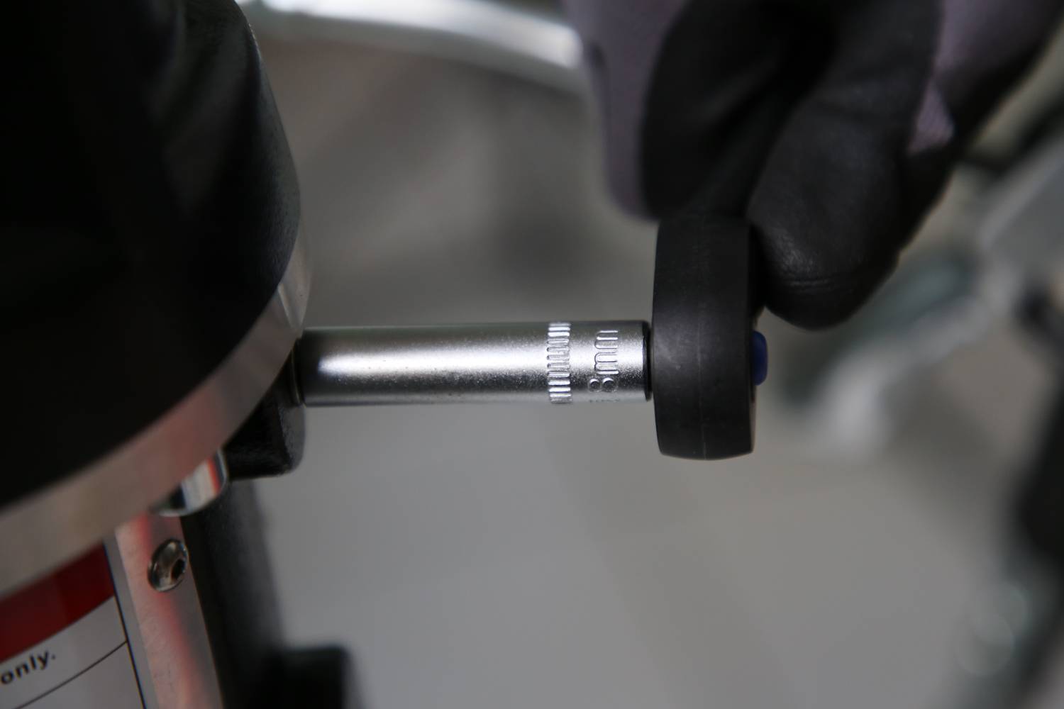 Ein Handschuh dreht einen silbernen Einstellknopf an einem Gerät, wobei feine Markierungen auf dem Knopf sichtbar sind.