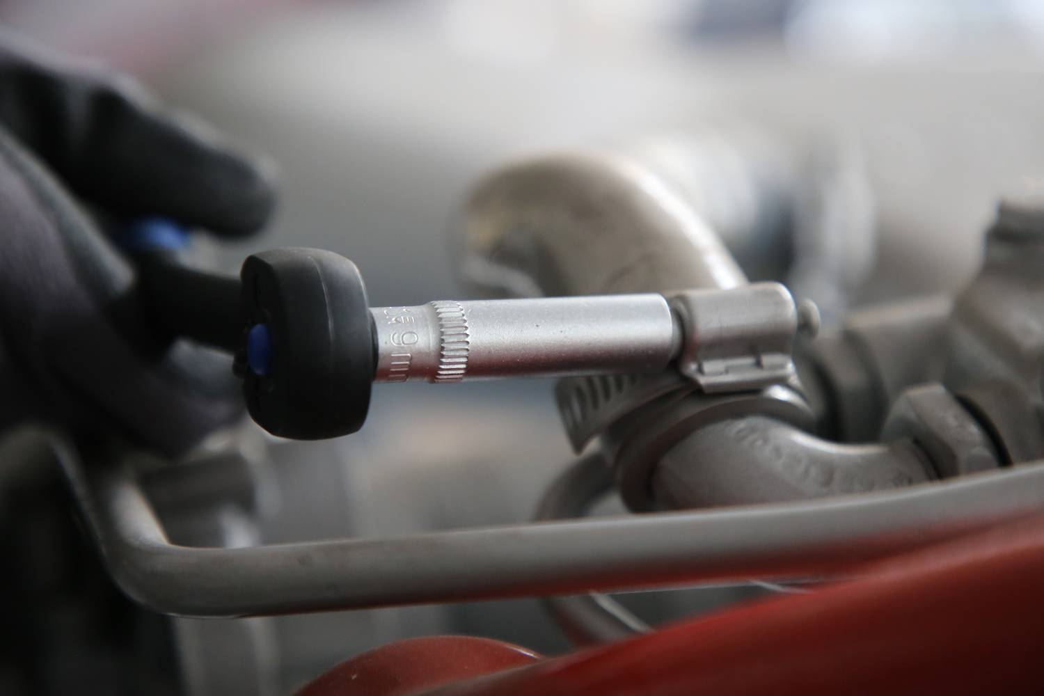 Eine Person misst den Reifendruck mit einem Druckmessgerät an einem Autoreifen. Der Fokus liegt auf dem Reifenventil und dem Messgerät.