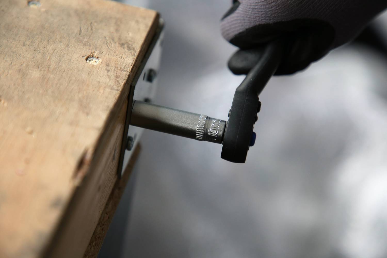 Eine Person zieht mit einem Schraubenschlüssel eine Schraube an einem hölzernen Werkstück fest.