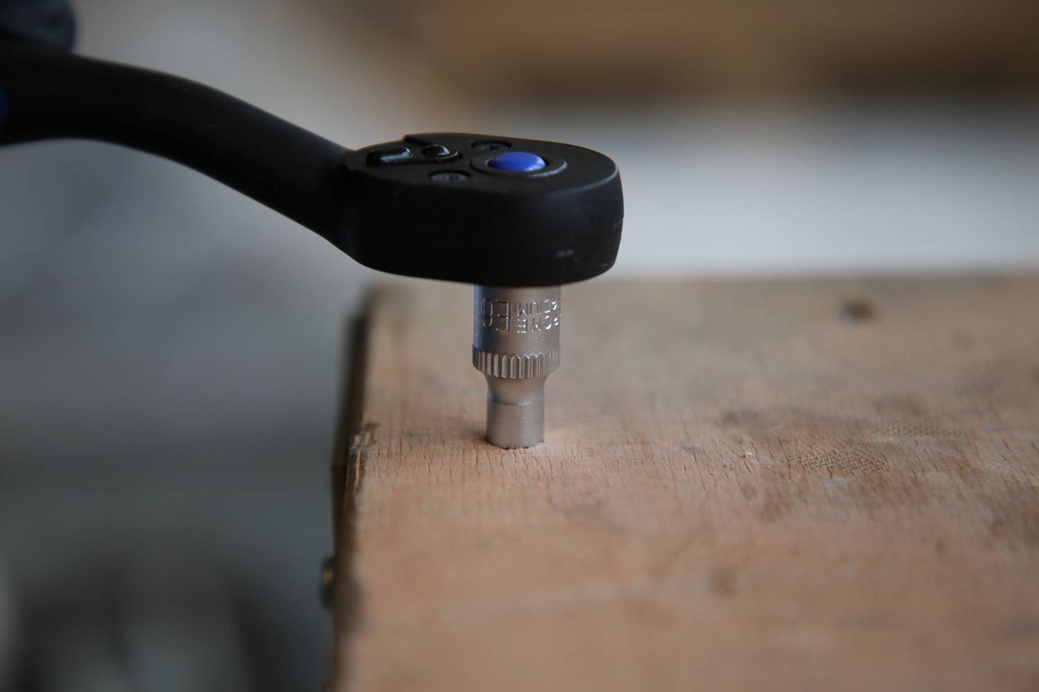 Nahaufnahme eines Ratschenwerkzeugs, das auf einem Holzbrett einen Schraubaufsatz dreht.