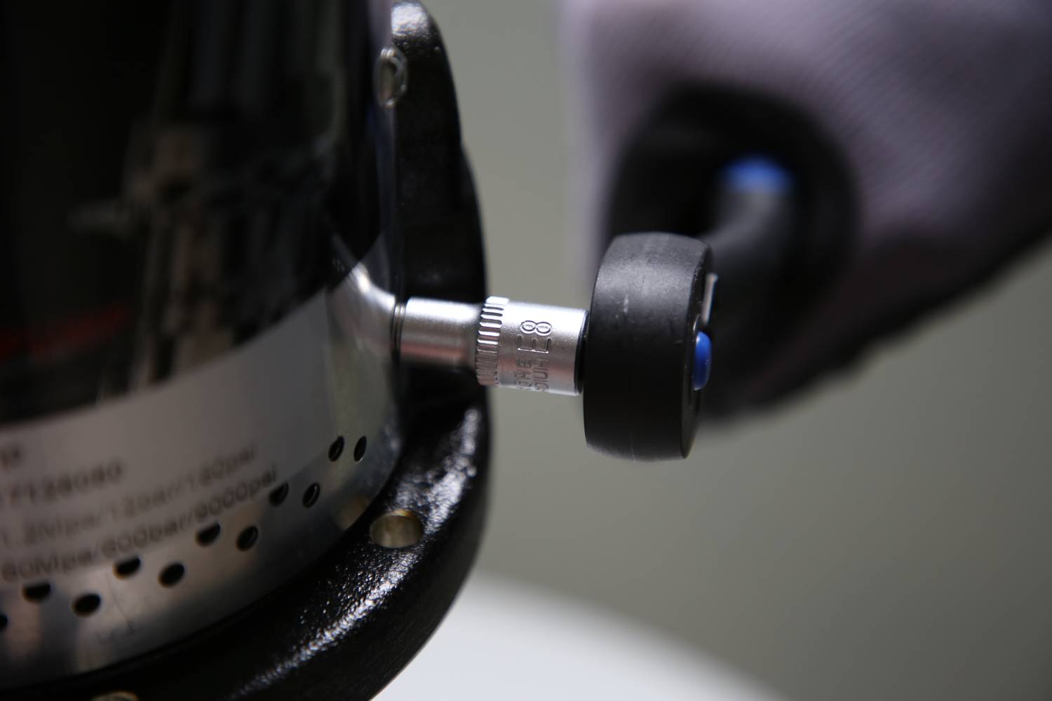 Nahaufnahme eines Werkzeugs mit einem Drehknopf, der von einer behandschuhten Hand gehalten wird. Der Fokus liegt auf dem Drehknopf.