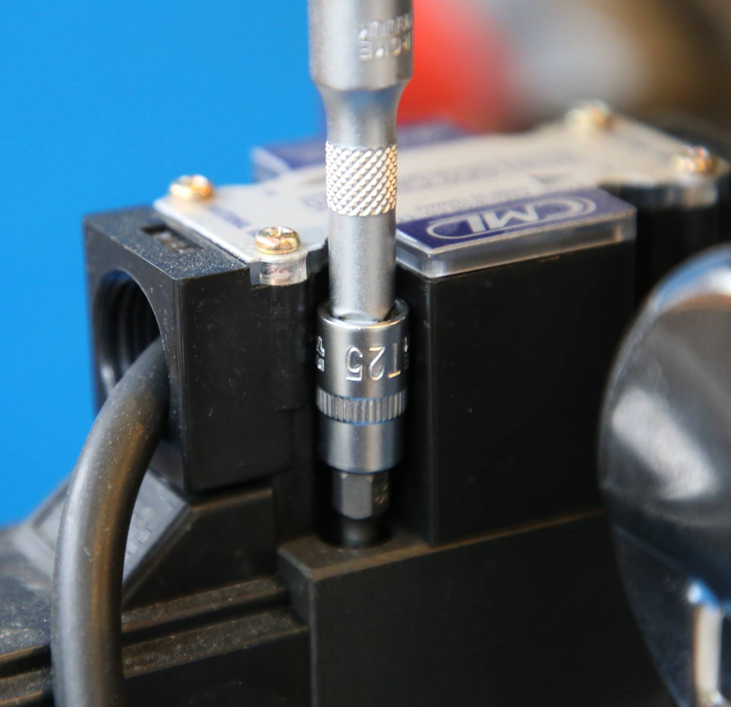 Ein Schraubenschlüssel fixiert eine Schraube an einem mechanischen Gerät mit einem Kabel im Vordergrund, blauer Hintergrund.