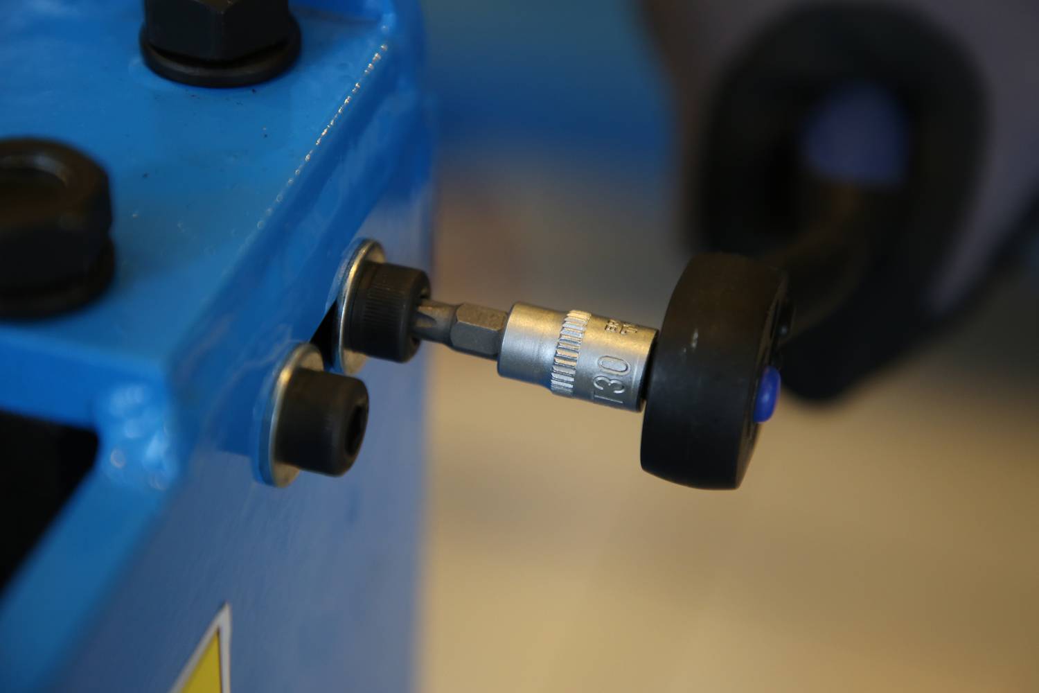 Eine handgehaltene Werkzeugspitze ist in eine Maschine oder einen Mechanismus eingesetzt, der blau gefärbt ist.