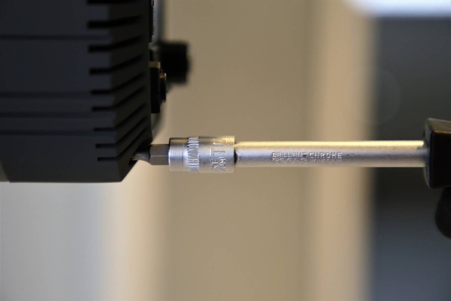 Ein Schraubendreher zieht eine Schraube in ein schwarzes Gerät fest. Der Fokus liegt auf dem Werkzeug und der Schraube.