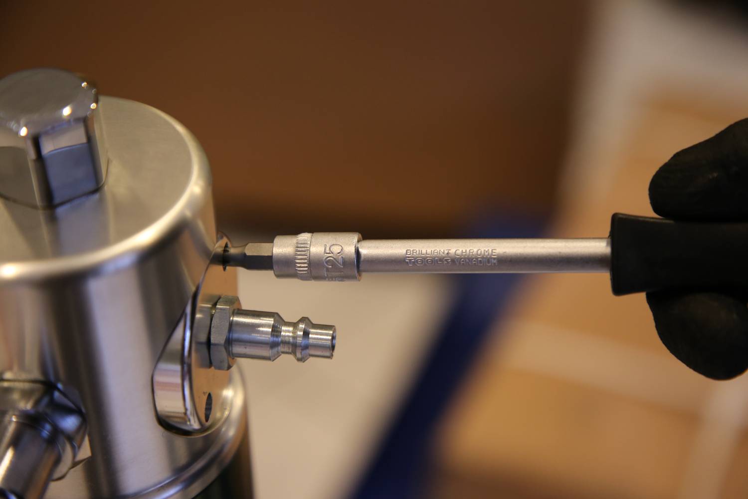 Eine Hand verwendet eine Ratsche, um eine Schraube an einem Metallgerät zu befestigen. Das Gerät hat verschiedene Anschlüsse.