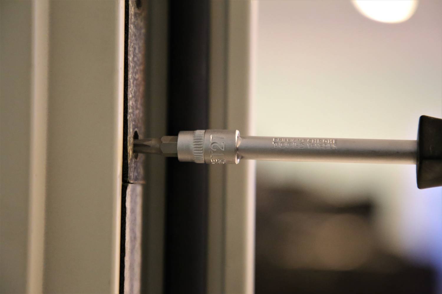 Ein Schraubenzieher wird in eine Schraube an einem Türrahmen gedreht, möglicherweise bei einer Reparatur oder Installation.