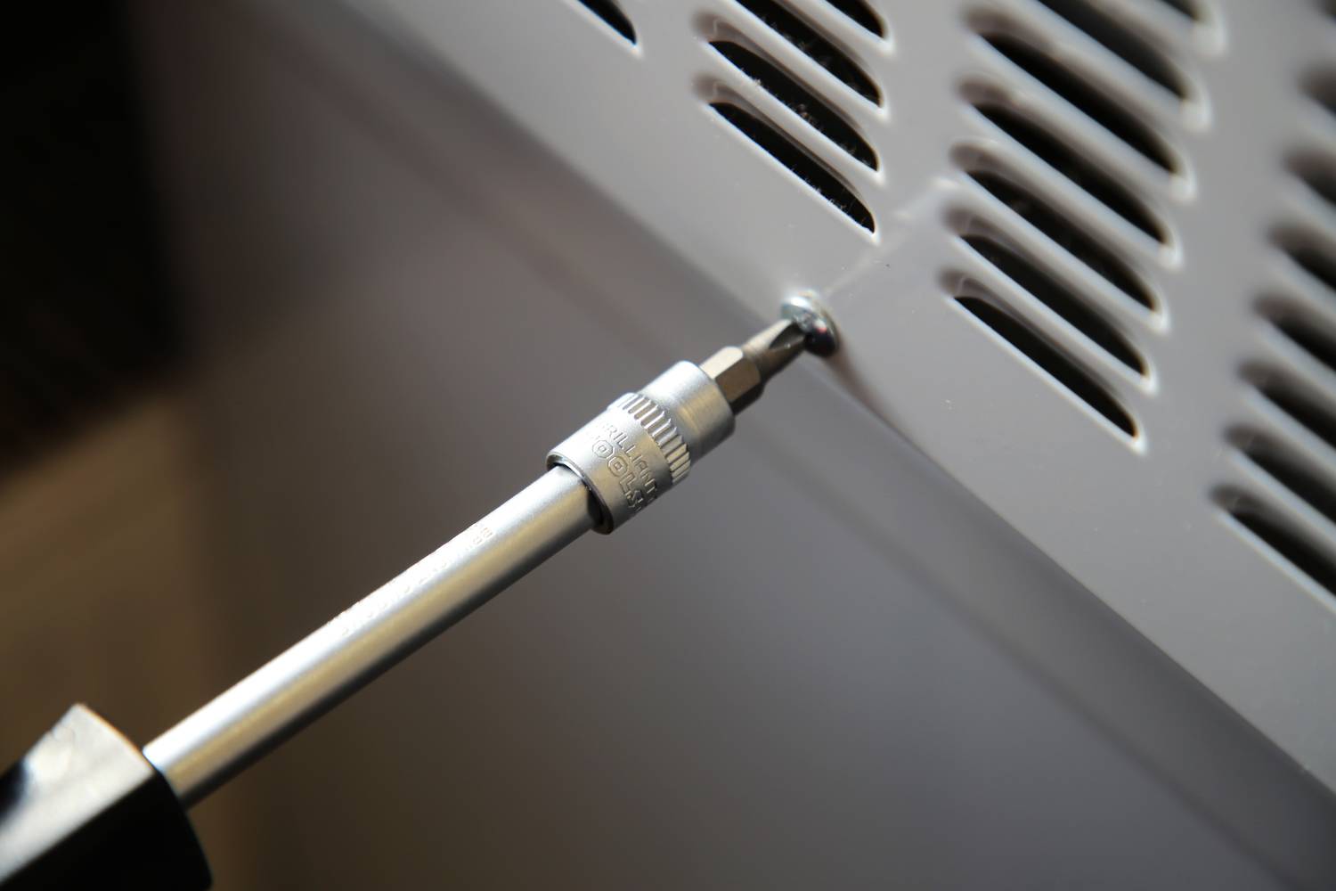 Ein Schraubendreher wird verwendet, um eine Schraube in einem metallischen Gitter festzuziehen.