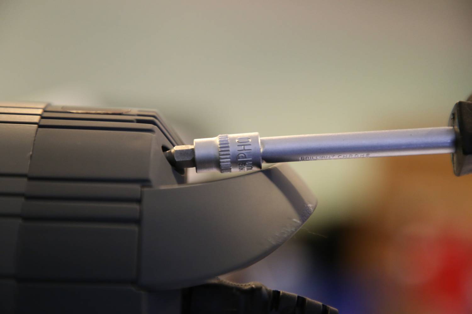 Nahaufnahme einer Person, die mit einem Schraubendreher eine Schraube dreht. Der Hintergrund ist unscharf.