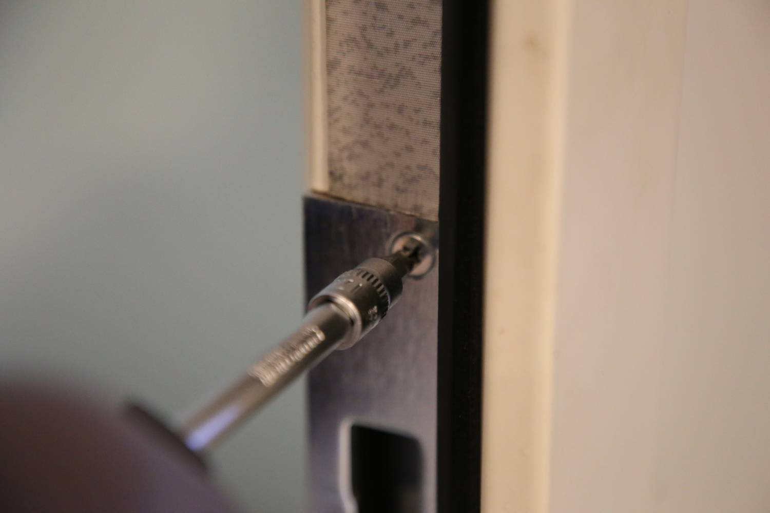 Nahaufnahme eines Schraubendrehers, der eine Schraube in einem Türscharnier anzieht.