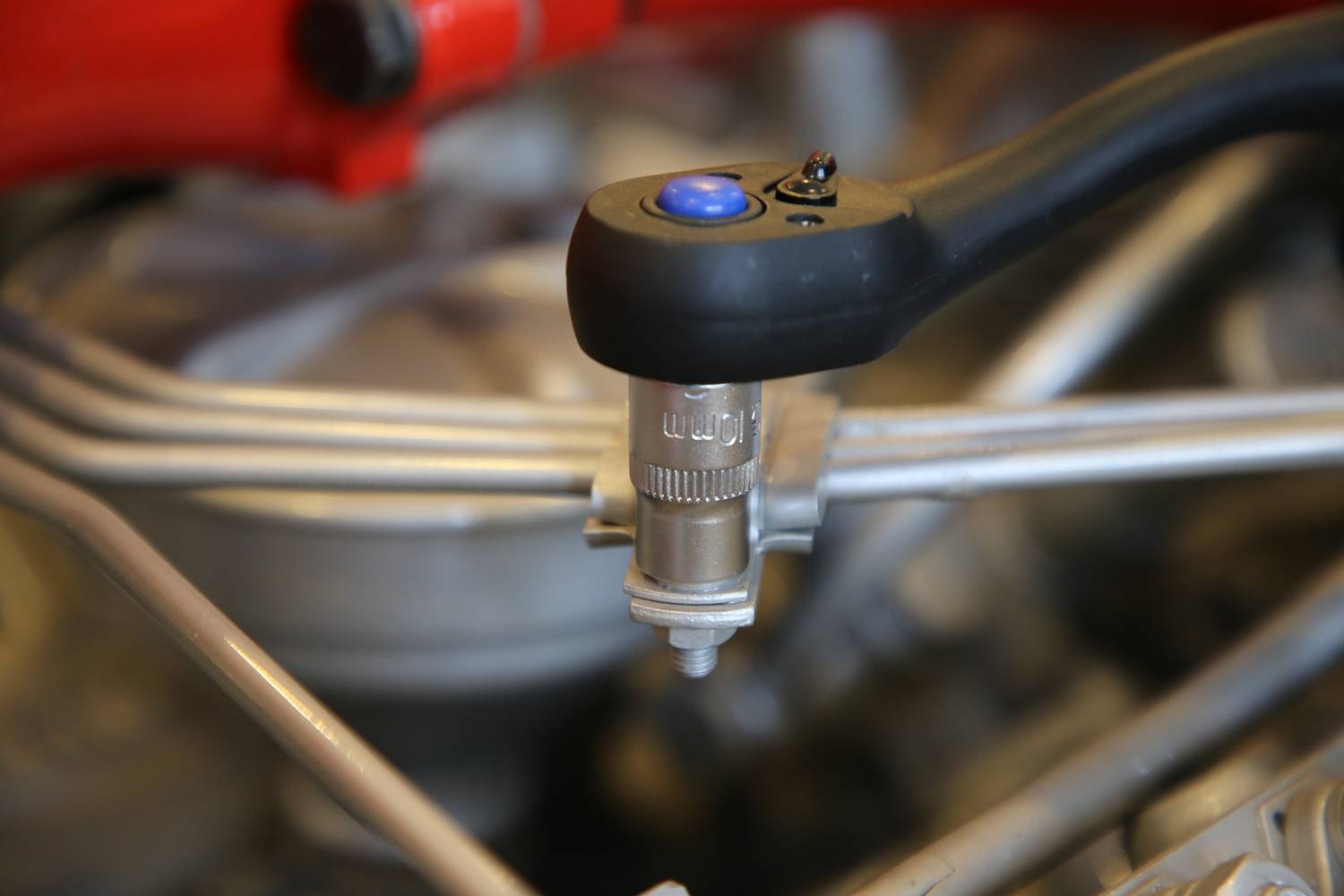 Nahaufnahme eines Drehmomentschlüssels, der an einer Schraube eines Autos arbeitet. Der Schlüssel hat einen blauen Knopf. Im Hintergrund sind Motorteile unscharf.