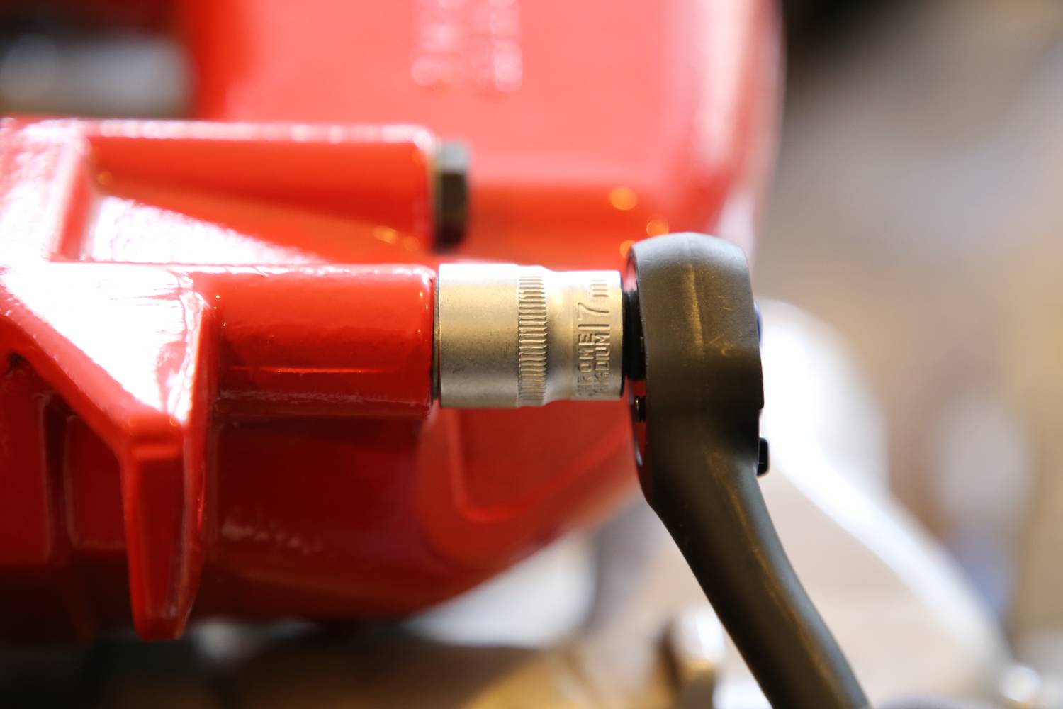 Nahaufnahme eines roten Bremssattels mit einem daran befestigten schwarzen Drehmomentschlüssel, der Spannung anzeigt.