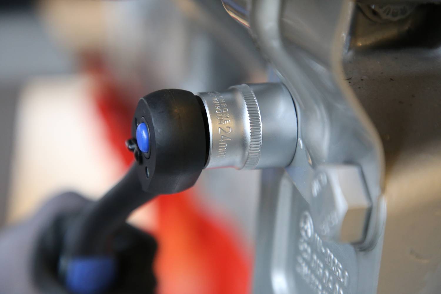 Eine Person hält einen Luftschlagschrauber, der auf eine Sechskantmutter an einem Fahrzeugmotor zielt, um diese zu lösen.