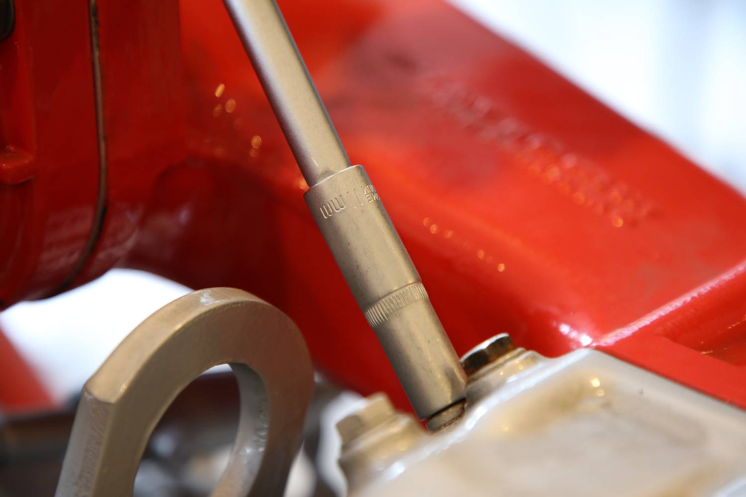 Ein silberner Schraubenschlüssel zieht eine Schraube an einem roten Metallgerät an. Nahaufnahme zeigt Details des Werkzeugs.