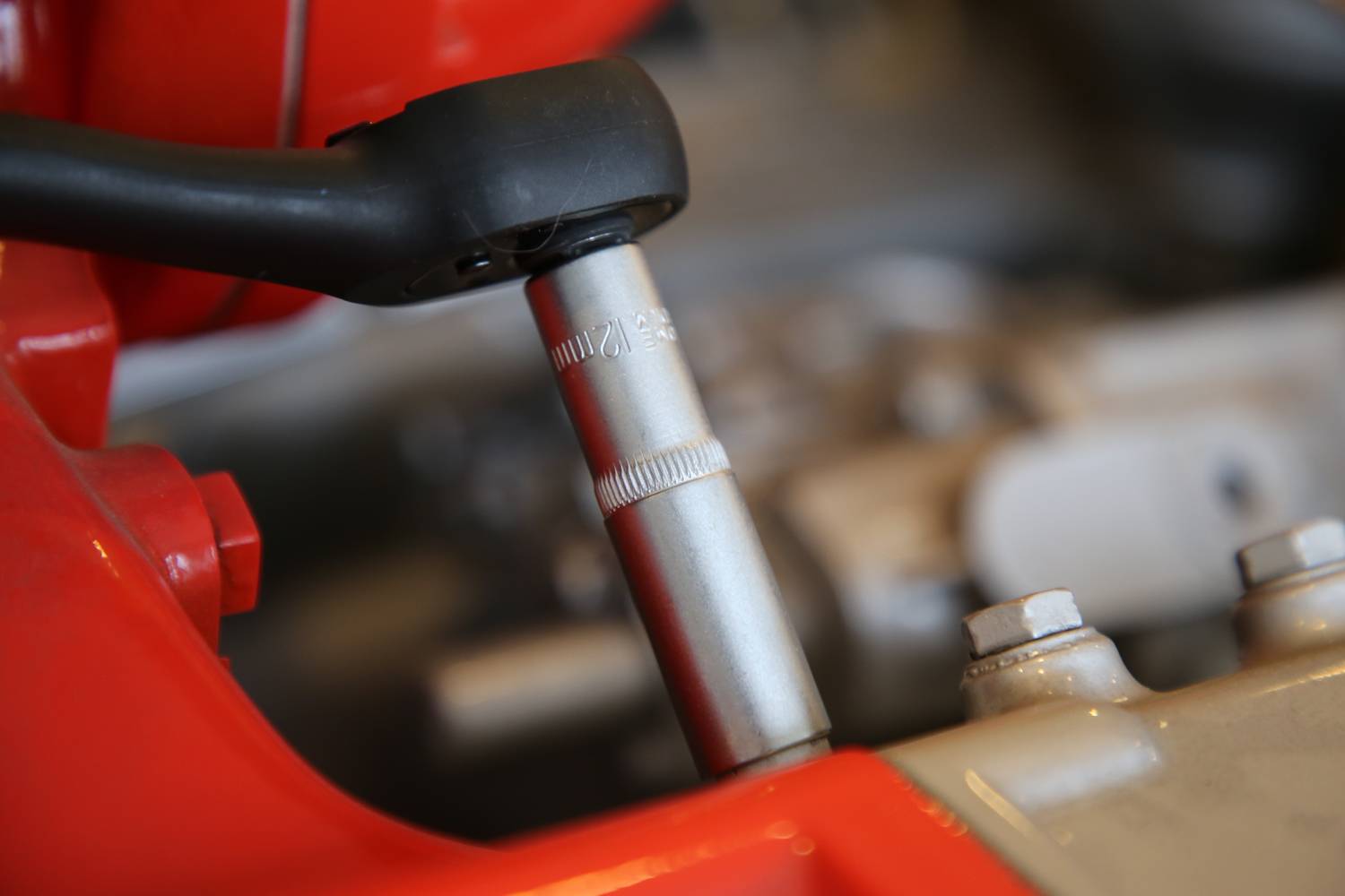 Nahaufnahme eines Werkzeugs, das eine Schraube an einem Maschinenmotor befestigt. Rote und silberne Bauteile sind sichtbar.