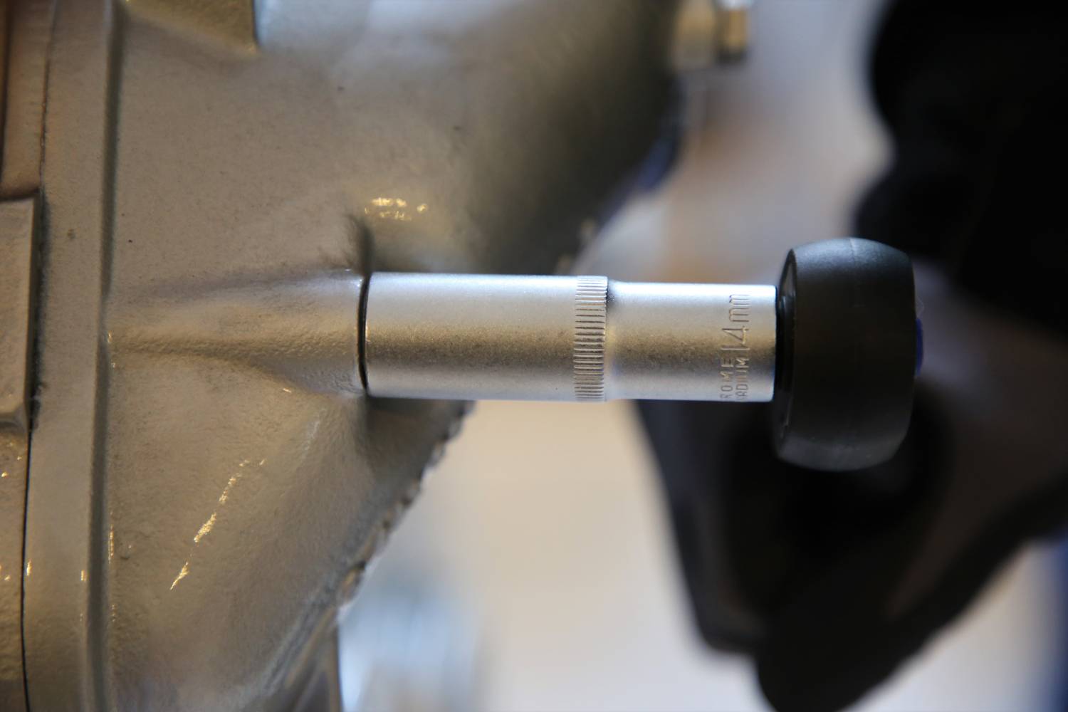 Ein silbernes Drehmomentwerkzeug wird von einer Person mit schwarzem Handschuh auf ein Metallteil angewendet, vermutlich zur Justierung.