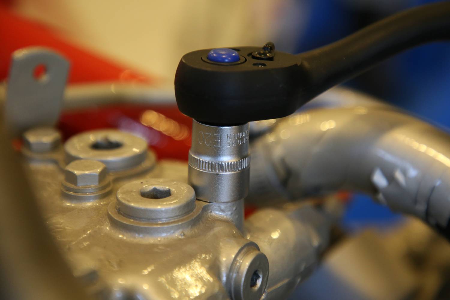 Eine Ratsche zieht eine Schraube an einem Metallteil an. Die Szene zeigt präzise Handwerksarbeit in einer technischen Umgebung.