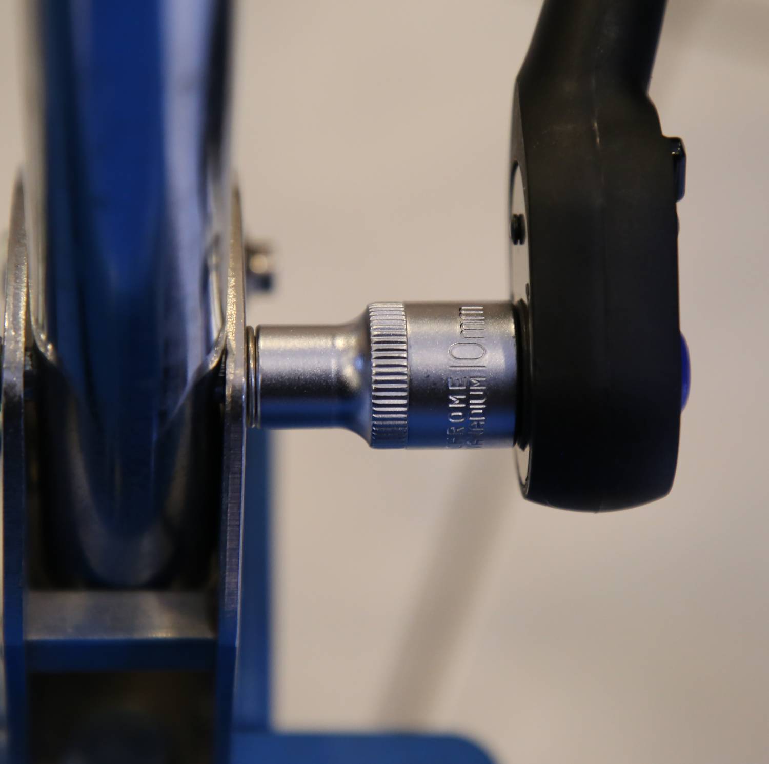 Nahaufnahme eines silbernen Werkzeugs mit Skala neben einem schwarzen Griff, das an ein blaues Metallobjekt angeschlossen ist.