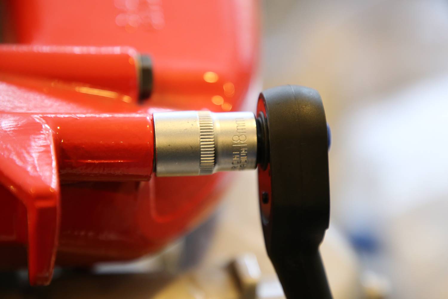 Nahaufnahme eines Ratschenwerkzeugs, das an einer Schraube eines roten Metallgehäuses angesetzt ist, Fokus auf die Gerätschäfte.