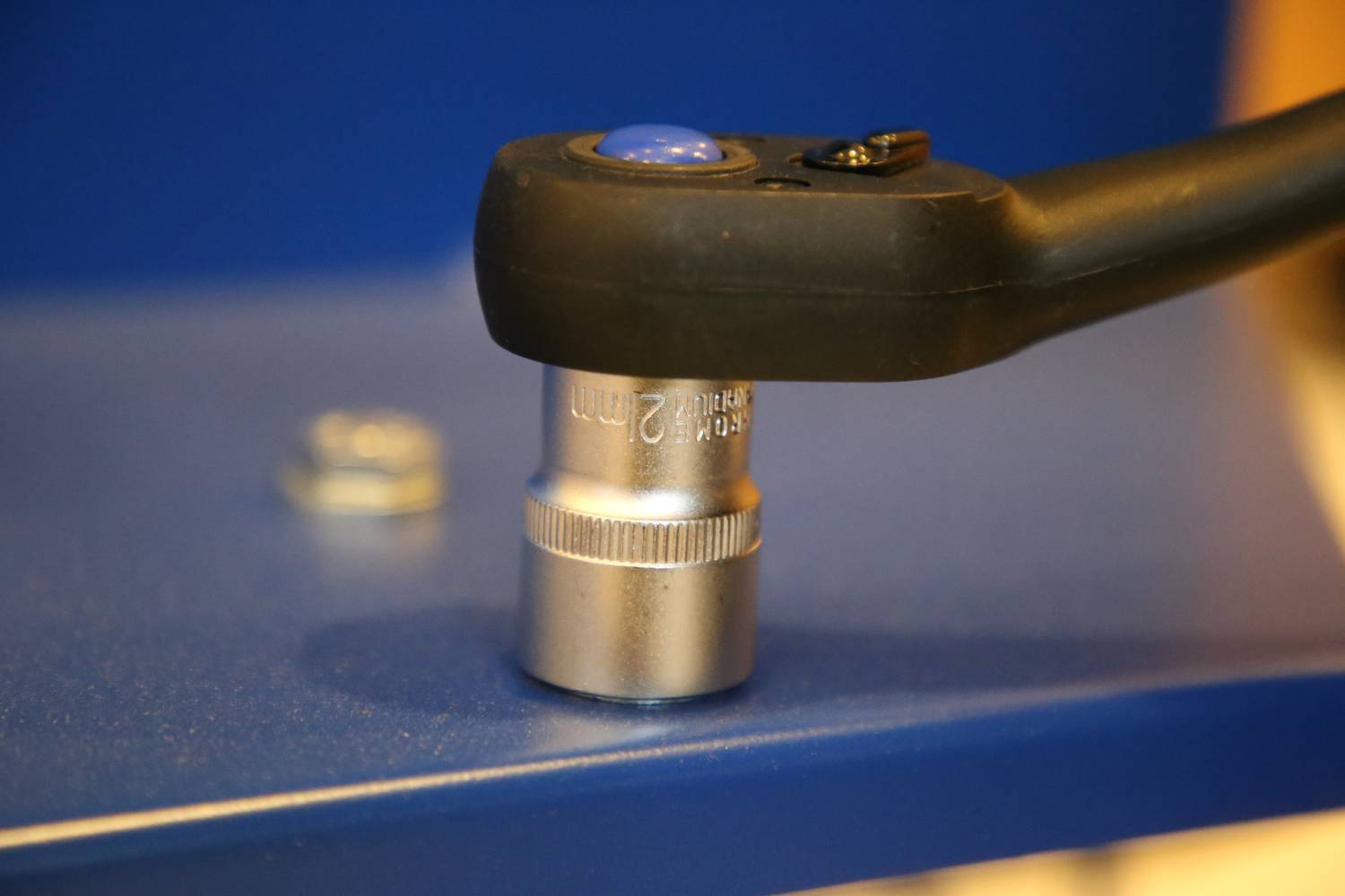 Ein Schraubenschlüssel mit 22mm Stecknuss ist auf eine blaue Oberfläche gelegt. Im Hintergrund ist eine weitere Schraube sichtbar.