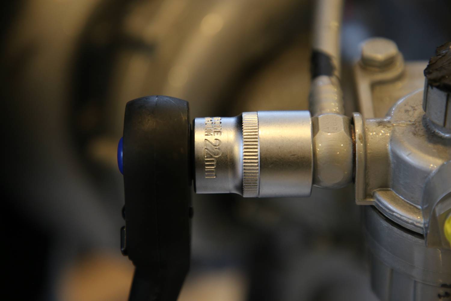 Nahaufnahme eines Metallventils mit einer schwarzen Drehknopfsteuerung, möglicherweise Teil einer Maschinen- oder Rohrinstallation.