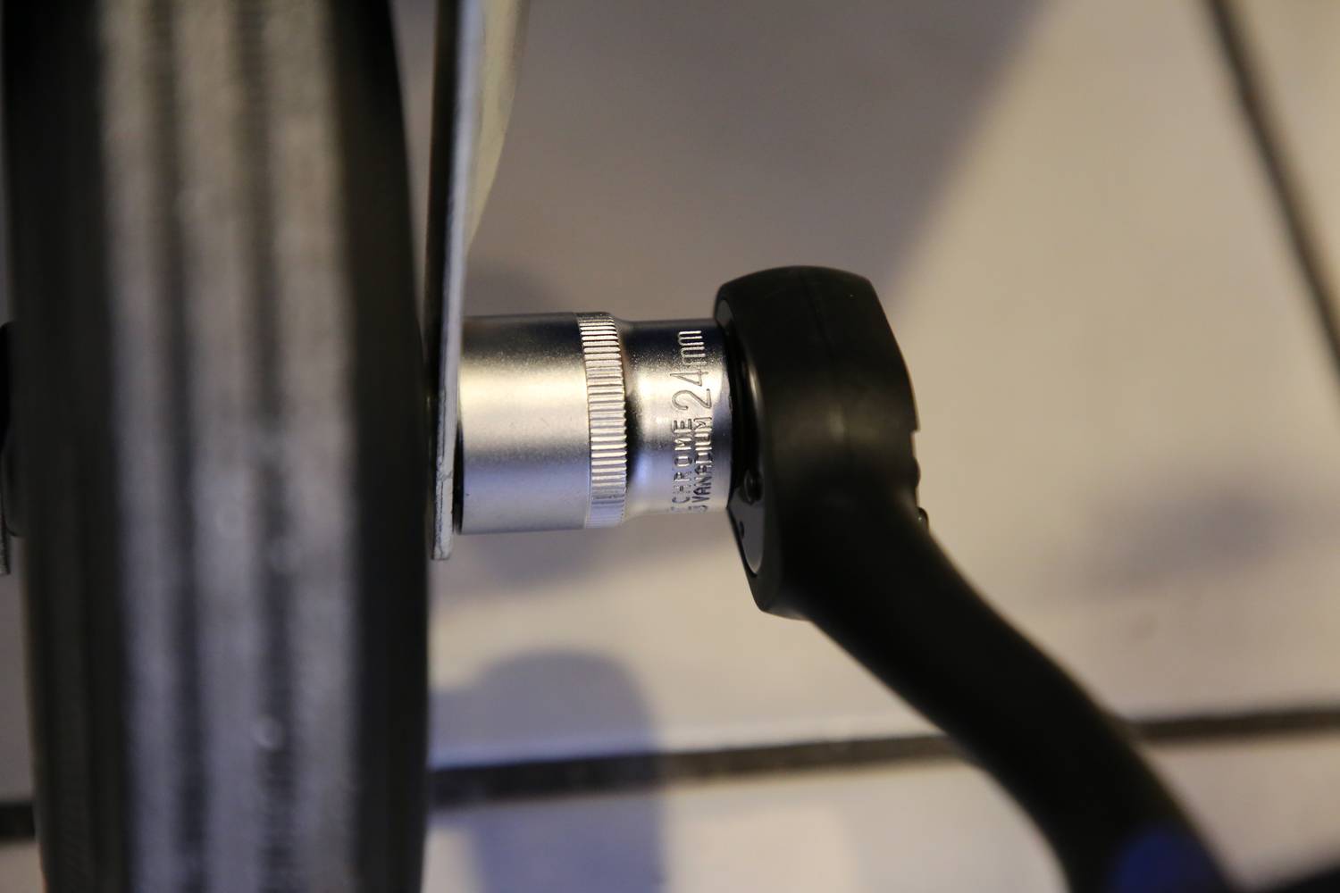 Ein Schraubenschlüssel ist an einer silbernen Mutter auf einer schwarzen Fahrradspeiche angesetzt.