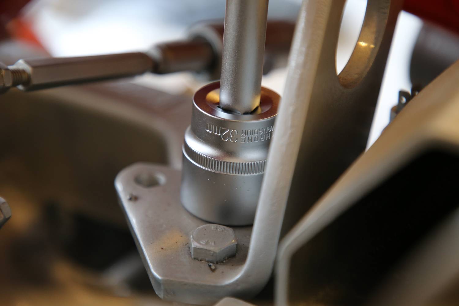 Ein silberner Schraubenschlüssel dreht eine Mutterschraube an einer Metallhalterung. Mechanikarbeit im Fokus.